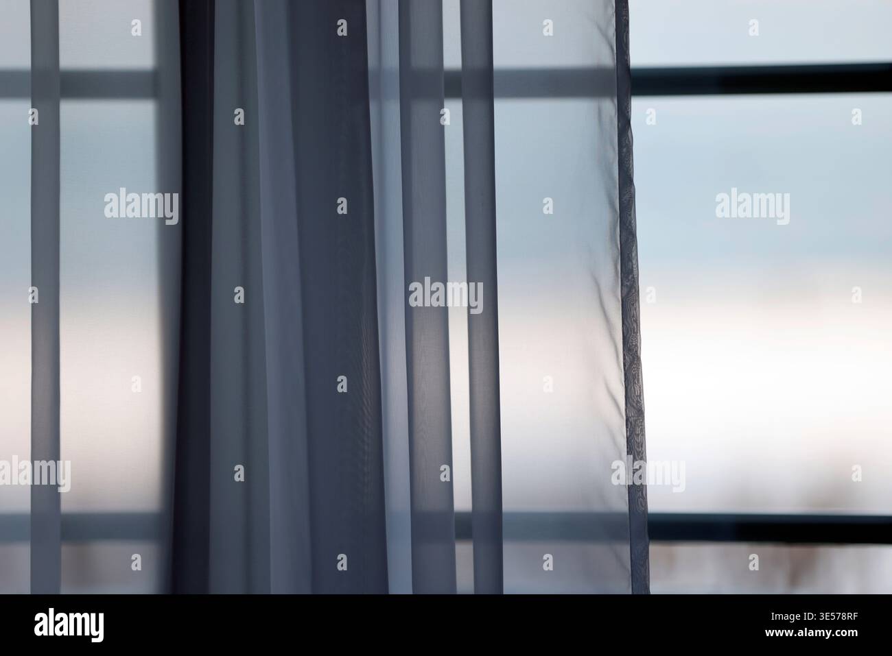 Transparente graue Vorhänge filtern sanftes Licht durch große Fensterrahmen und schaffen ruhige, mehrschichtige Schleier im modernen Innenraum. Sopot. Polen. Stockfoto