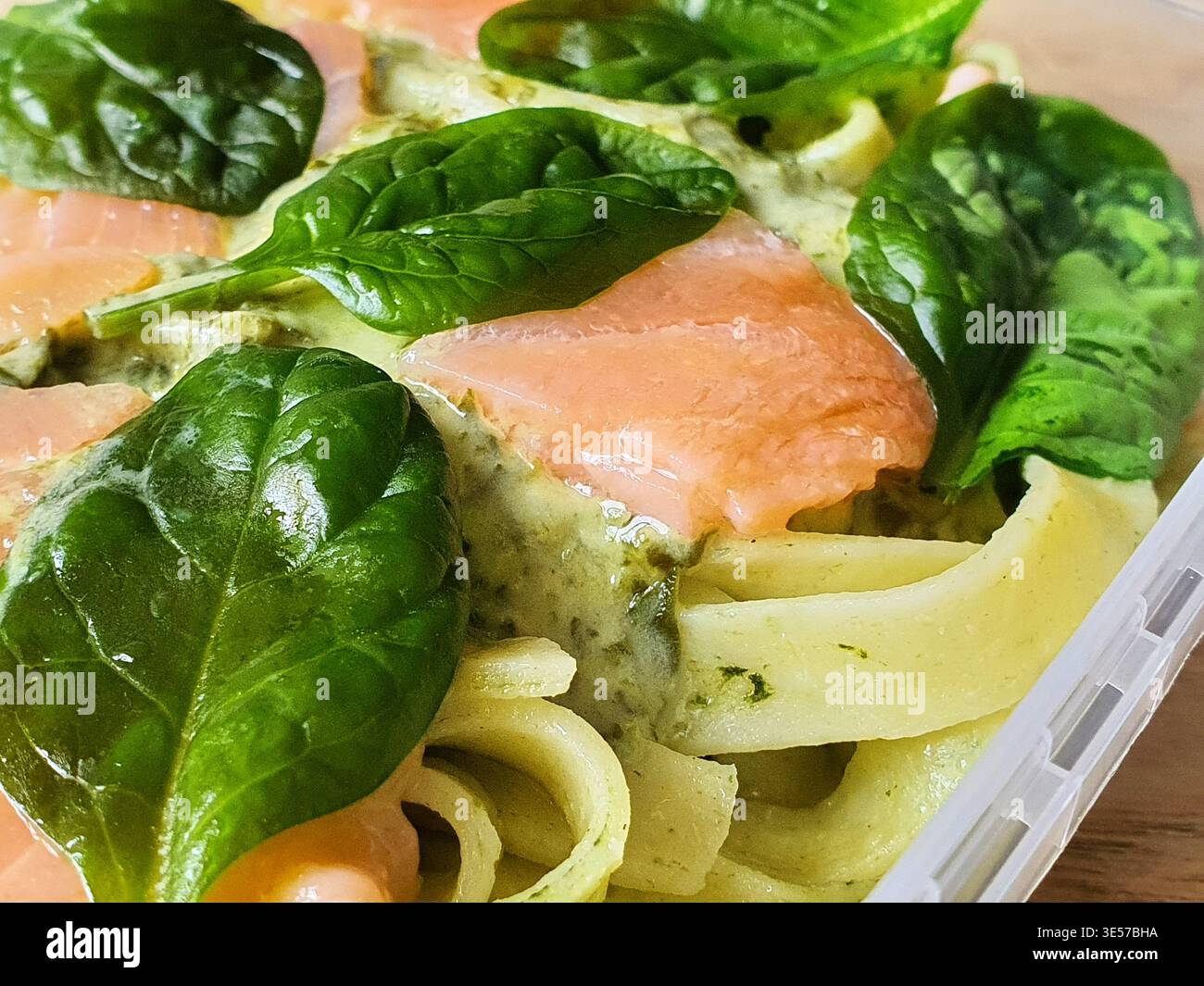 Makrofoto aus Nahaufnahme eines zubereiteten Pastagerichts mit flachen Bandnudeln, wahrscheinlich Fettuccin oder Tagliatelle, überzogen mit einer cremigen grünen Sauce. Stockfoto