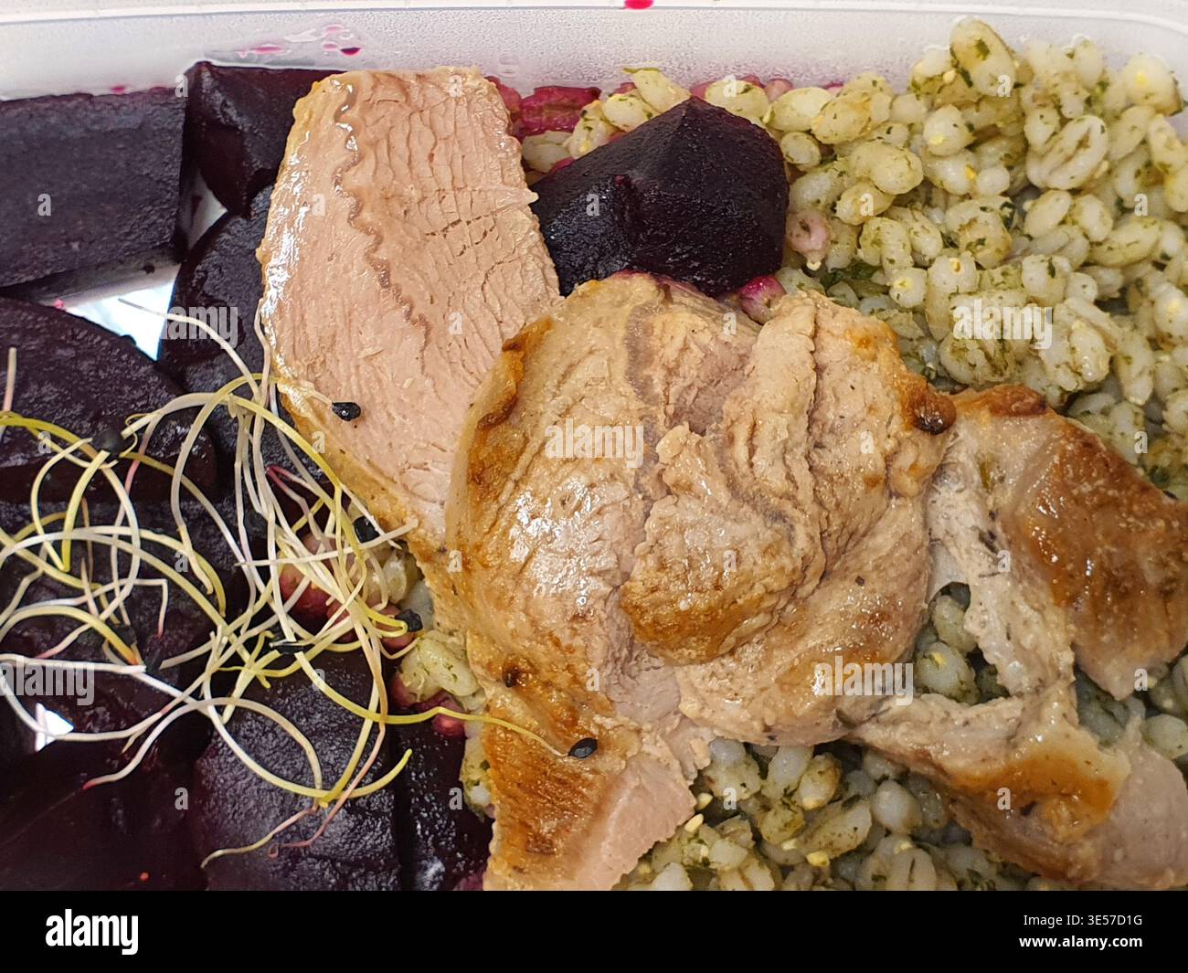 Eine Nahaufnahme einer zubereiteten Mahlzeit, die in einem weißen Kunststoffbehälter serviert wird. Das Gericht besteht aus mehreren gerösteten Fleischscheiben mit gebräunten, Stockfoto