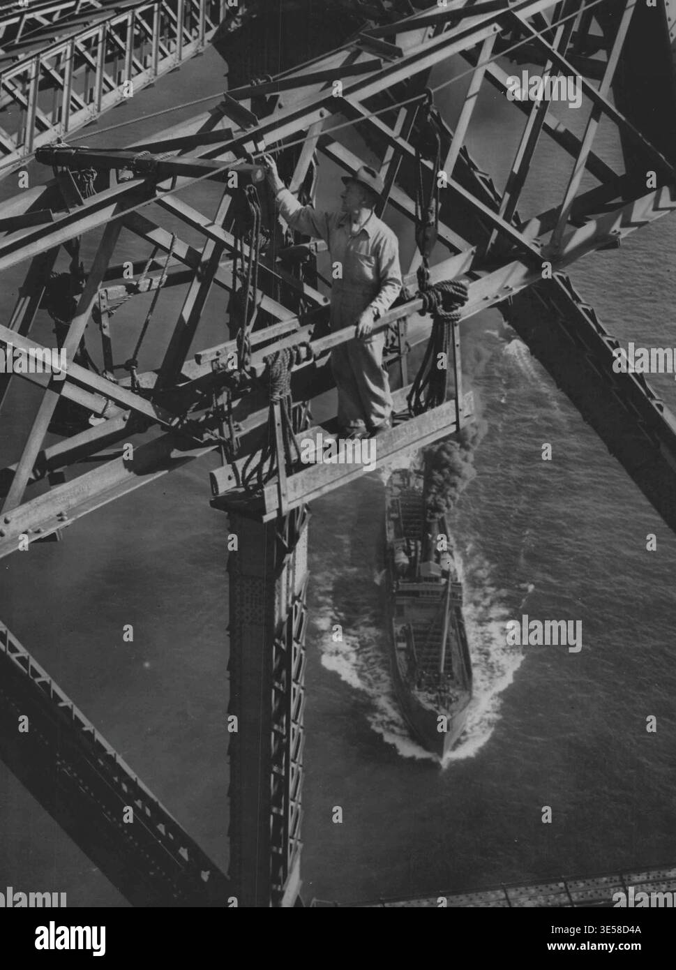 Takelage – Maler bauen eigene Bühnen mit getestetem manila-Seil oder -Draht. Hier gab es keine Todesopfer durch Versagen der Lackiergeräte seit der Eröffnung der Brücke im Jahr 1932. Eine gute Bilanz. Nur wenige der Tausenden von Menschen, die täglich Sydneys gigantische Harbor Bridge überqueren, merken, dass über ihren Köpfen wie Spinnen in einem riesigen Netz die Männer der Bridge Painting Gang schwingen. Außer bei nassem oder windigem Wetter, wenn sie unter der Decke arbeiten, lackieren diese Männer kontinuierlich, bis sie mehr als 800 Gallonen erstklassige Farbe auf die 50.000 Tonnen Stahlarbeiten aufgetragen haben. Dann fangen sie von vorne an, um das nächste coa zu verbreiten Stockfoto