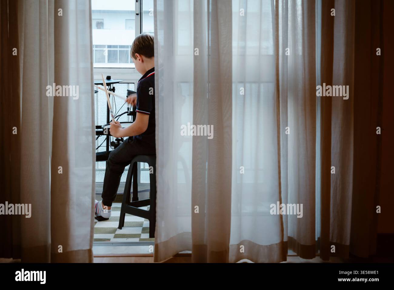 Junge spielt elektronische Trommeln auf dem Balkon zu Hause, Kind übt Musik Stockfoto