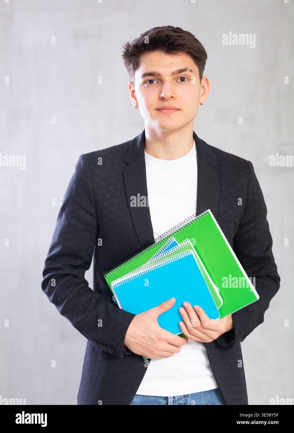 Junger männlicher Wissenschaftler in Jackentüchern mit einem großen Stapel Noten an der grauen Wand. Stockfoto