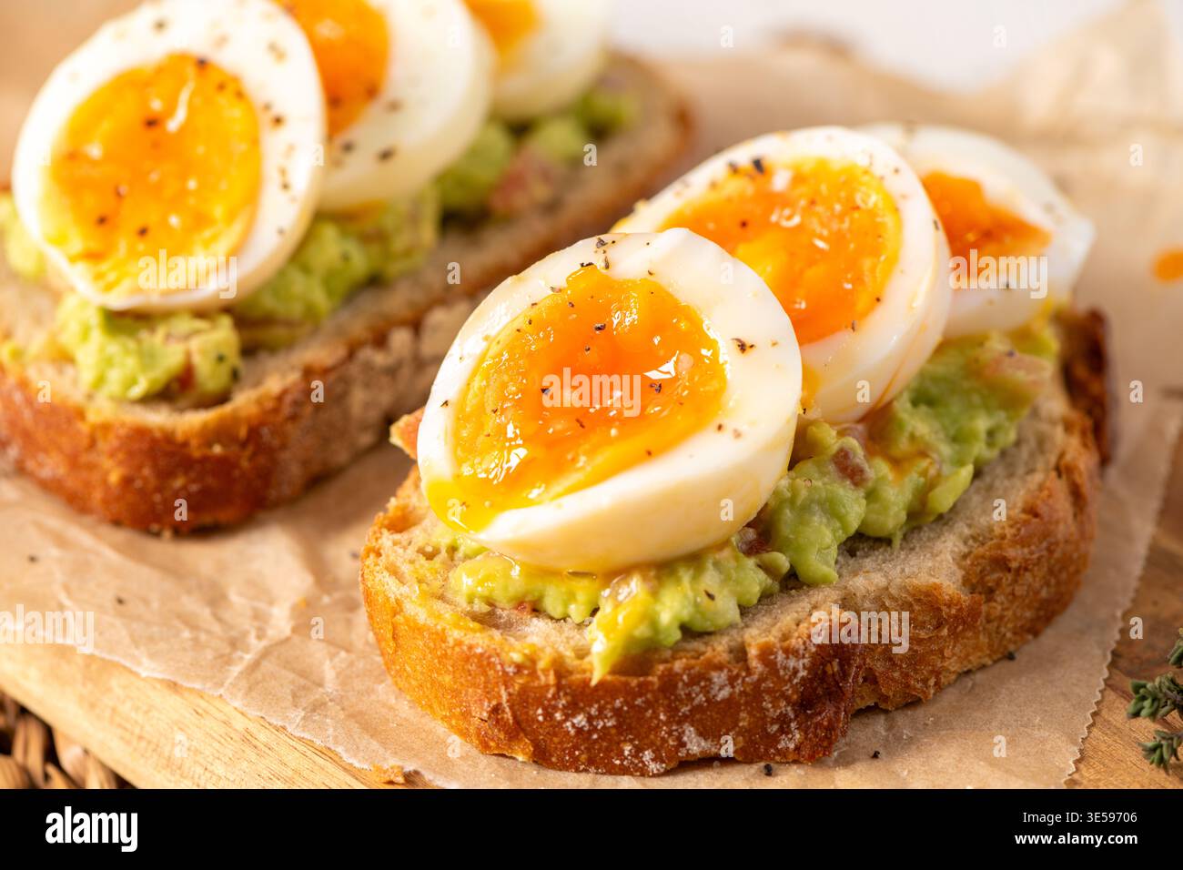 Zwei Scheiben knuspriger Sauerteig, belegt mit Avocadopüree und marmelierten weichen gekochten Eiern. Warme, natürliche Beleuchtung hebt die cremige Dotterstruktur und cra hervor Stockfoto