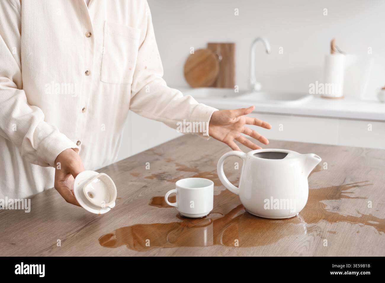 Frau mit Tasse, Topf und verschüttetem Kaffee auf dem Tisch in der Küche Stockfoto