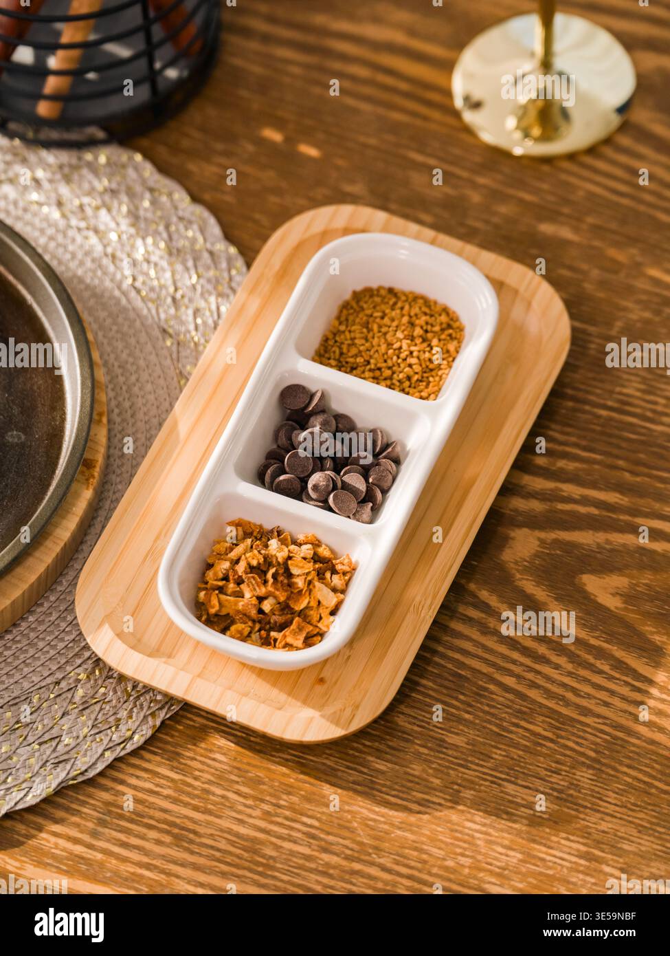 Ein weißer, mit Schokoladenchips und Gewürzen gefüllter, geteilter Keramikserver wird in weichem Licht auf einer Holzplatte platziert. Stockfoto