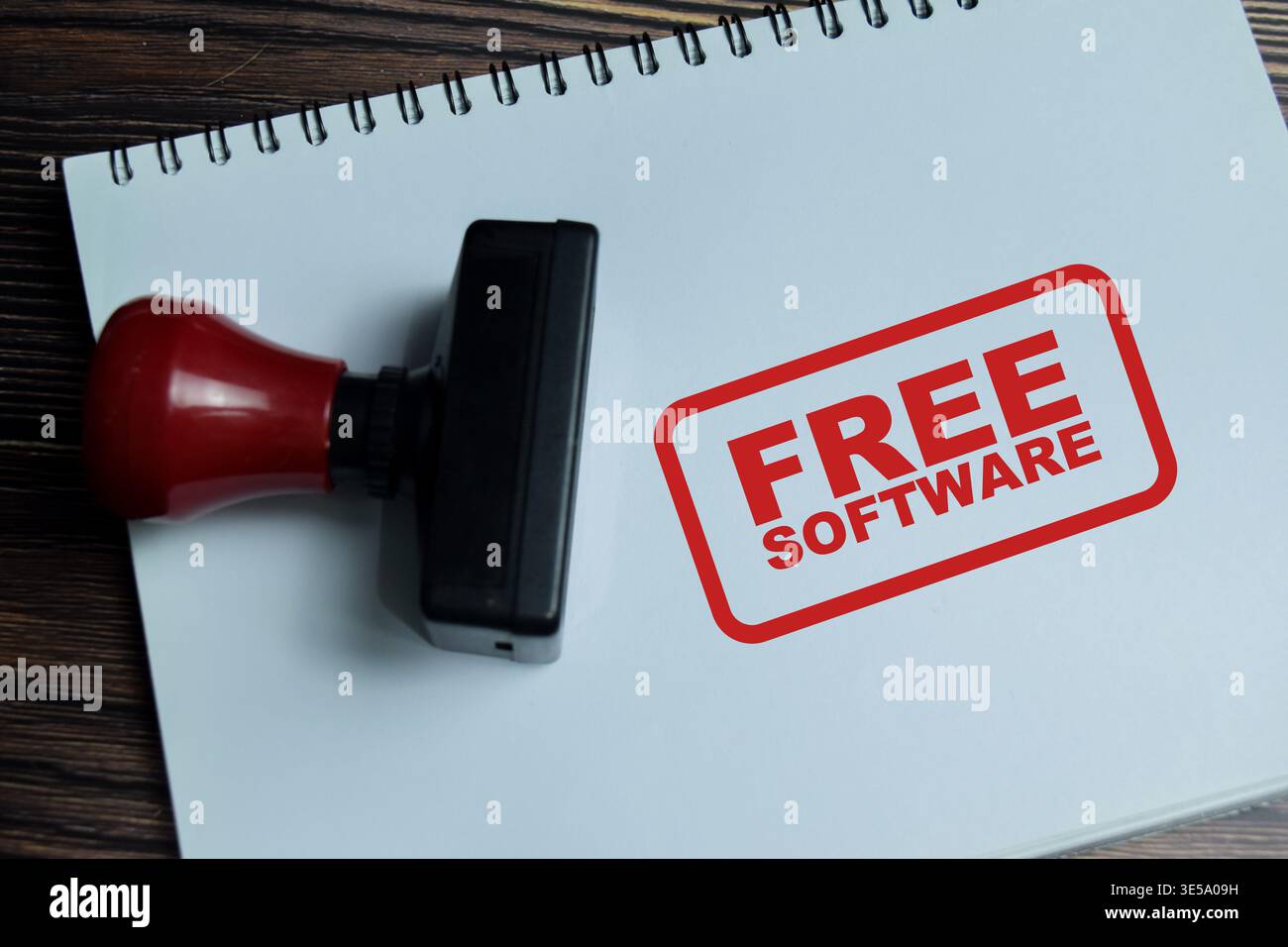 Roter Griff Gummistempel und kostenloser Software-Text über dem Buch isoliert auf hölzernem Hintergrund. Für Open Source- oder kostenlose Programme Stockfoto