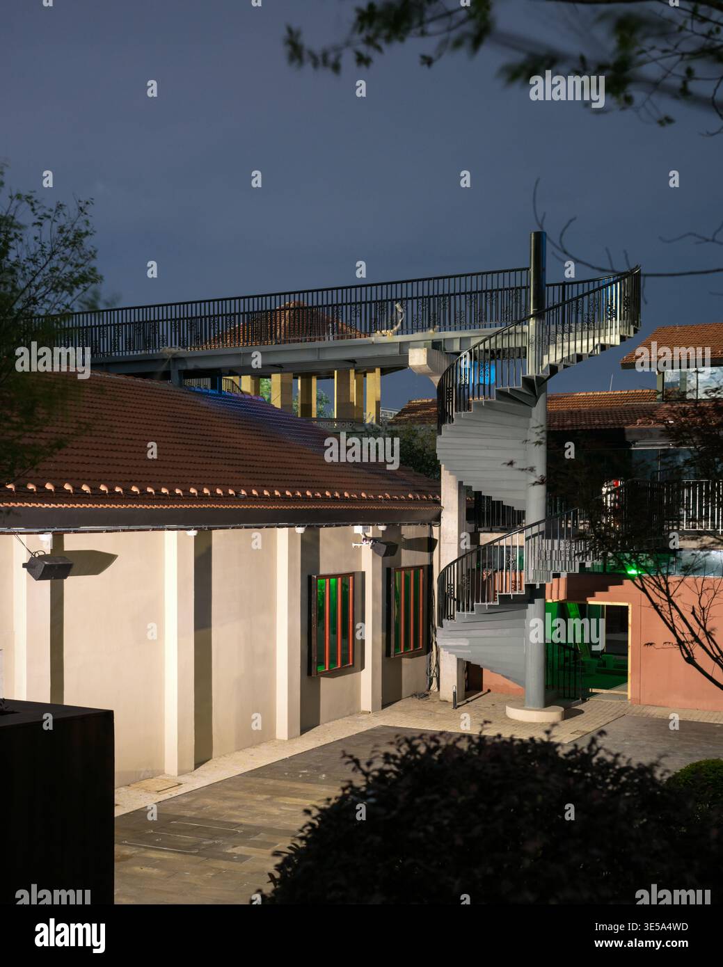 Großer Blick auf einen leeren gepflasterten Innenhof mit einer Wendeltreppe aus Metall und einem erhöhten Fußgängerweg, der die renovierten Gebäude verbindet. Erfasst V Stockfoto