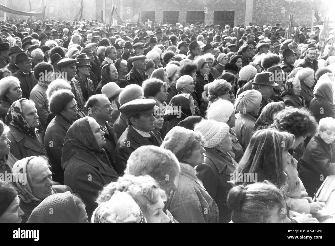 Sloviansk, 7. November 1996, Lenin Park (heute Shovkowytschyj). Während einer politischen Kundgebung im Herbst steht eine dichte Menge von Senioren und Anwohnern im Freien. Die dicht gepackten Menschen, die in schweren Wintermänteln und diversen Kopfbedeckungen gekleidet sind, blicken gleichmäßig auf einen Lautsprecher außerhalb der Kamera. Im fernen Hintergrund ist ein gemauertes Gebäude schwach sichtbar. Dieses authentische Schwarz-weiß-Archivbild fängt die fokussierten Ausdrucksformen der Gemeinschaft ein und spiegelt das Leben vor dem Krieg im friedlichen Donbass wider. Stockfoto