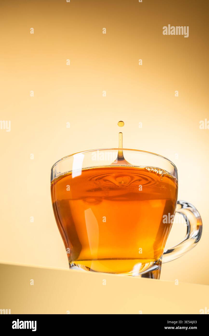 Glasbecher Tee mit tropfendem Tropfen auf gelbem Hintergrund Stockfoto