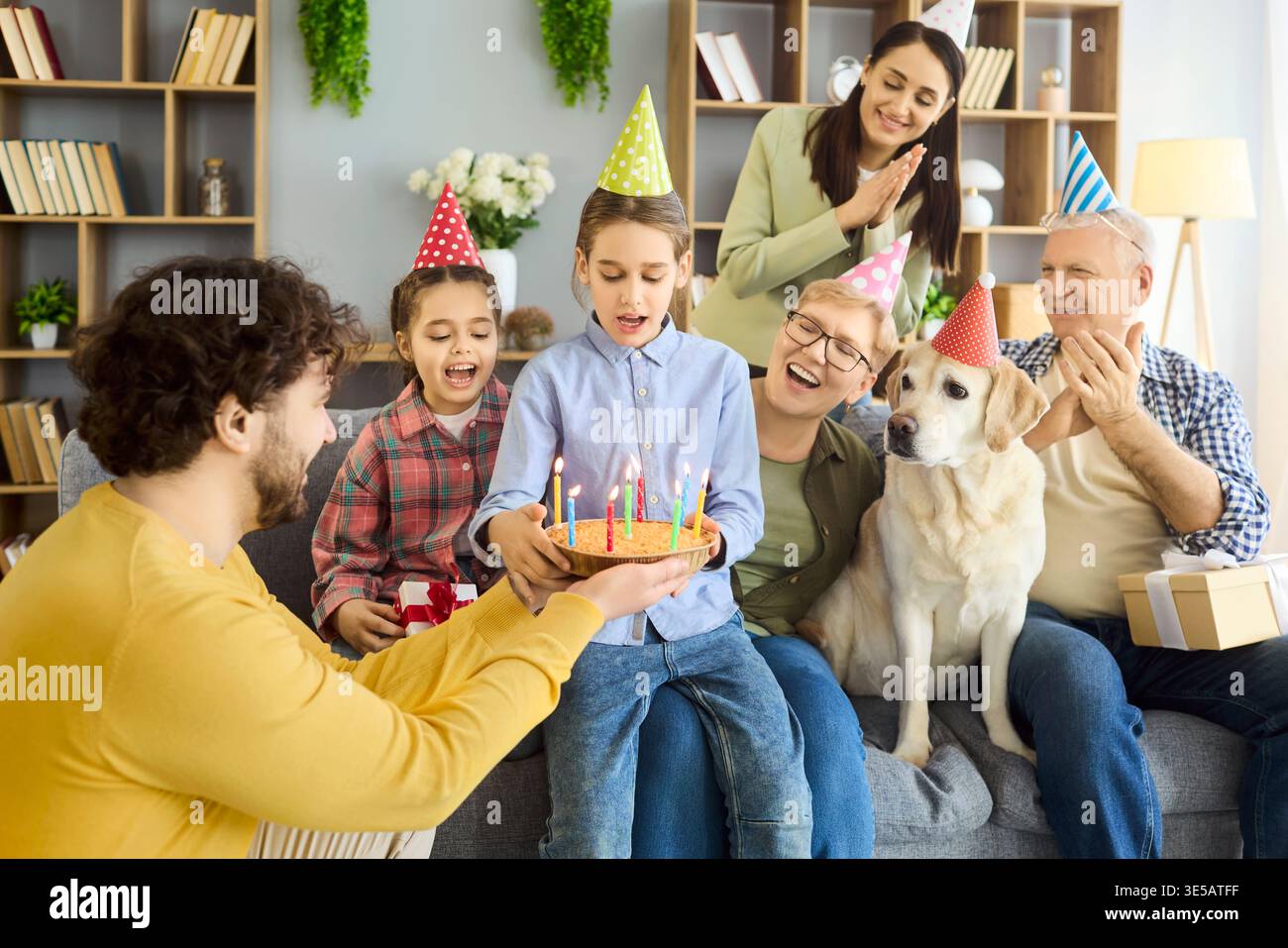 Mehrgenerationengeburtstag zu Hause mit Kuchen, Kerzen, Geschenken und Hund Stockfoto