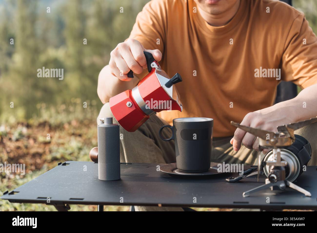 Eine Person aus der Nähe, die Kaffee aus der Mokakanne in eine Tasse gießt, während sie in der Natur im Freien campt Stockfoto