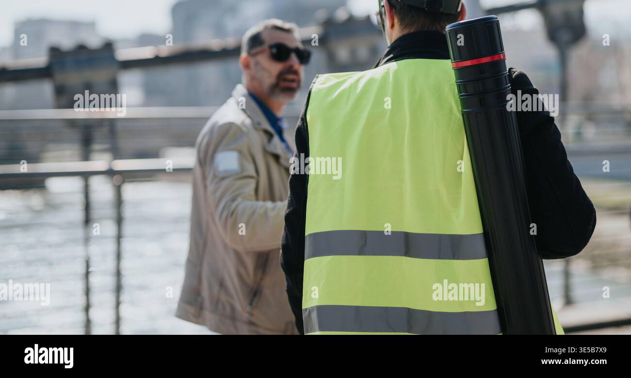 Bauarbeiter in Warnweste spricht mit Kollegen am Wasser mit Blaudruckrohr Stockfoto