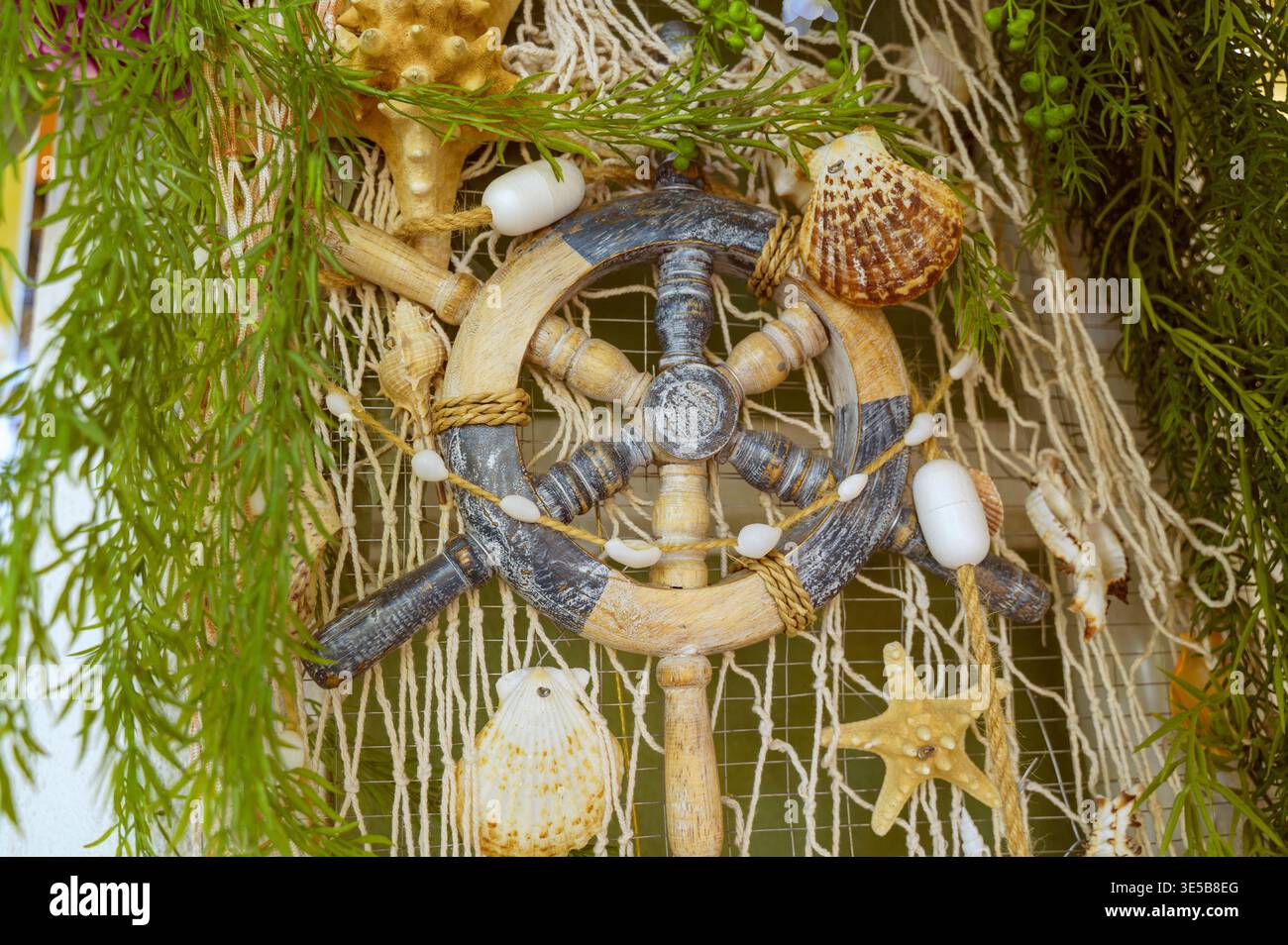 Dekoratives Schiffslenkrad mit Muscheln und Fischernetz. Stockfoto