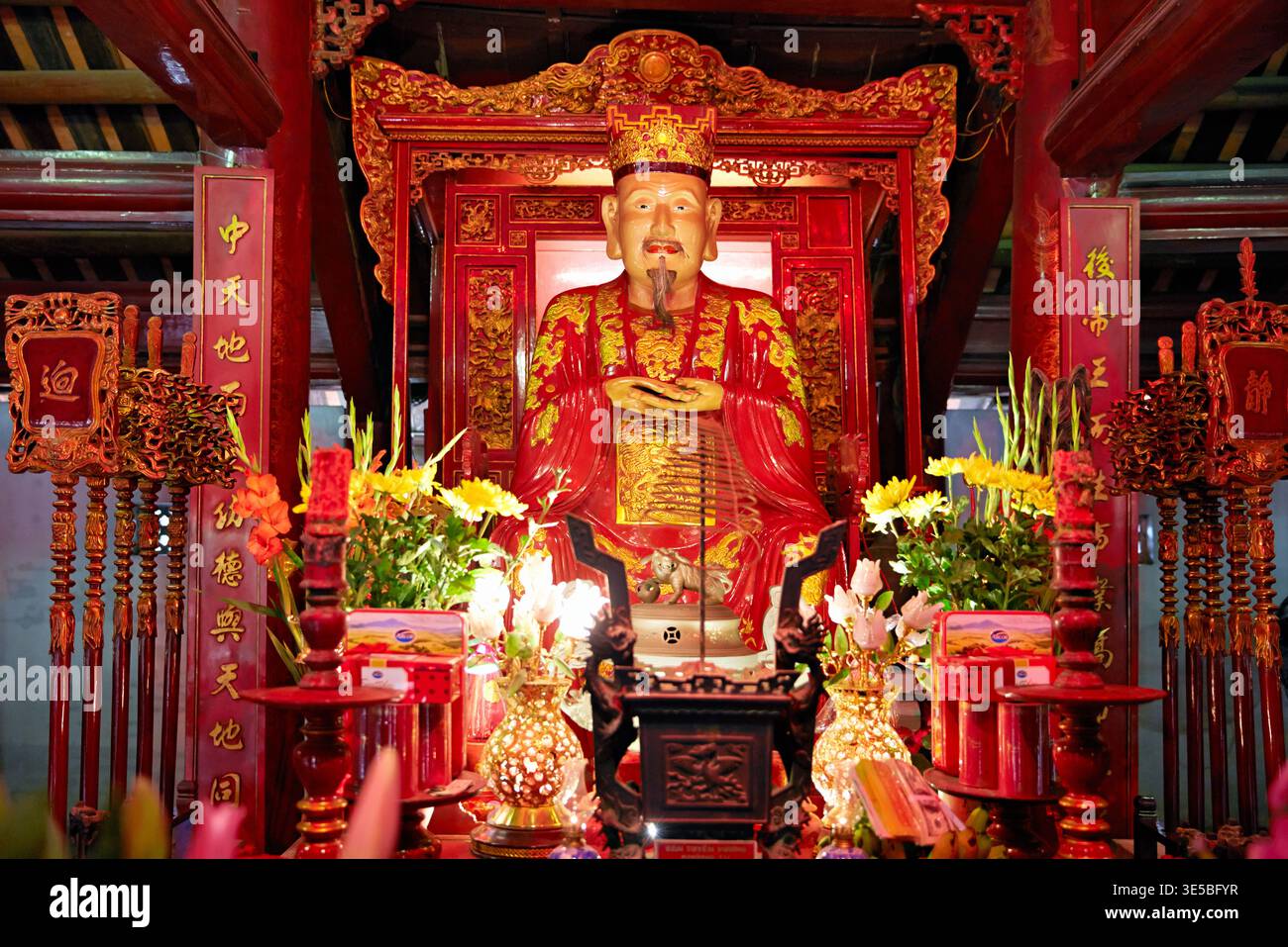 Eine große Statue steht in einem Tempel in Hanoi. Blumen und Kerzen umgeben die Statue und verleihen dem Raum Farbe und Licht. Stockfoto