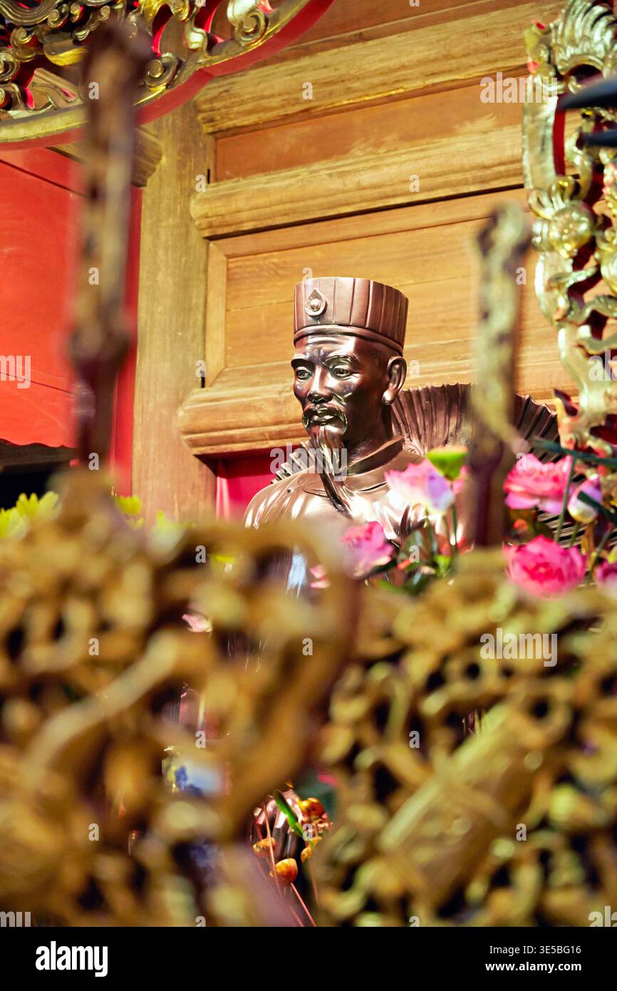 Eine Bronzestatue steht in einem Tempel in Hanoi. Es zeigt eine Figur, die starke Symbole der vietnamesischen Kultur hält. Besucher beobachten das Kunstwerk genau. Stockfoto