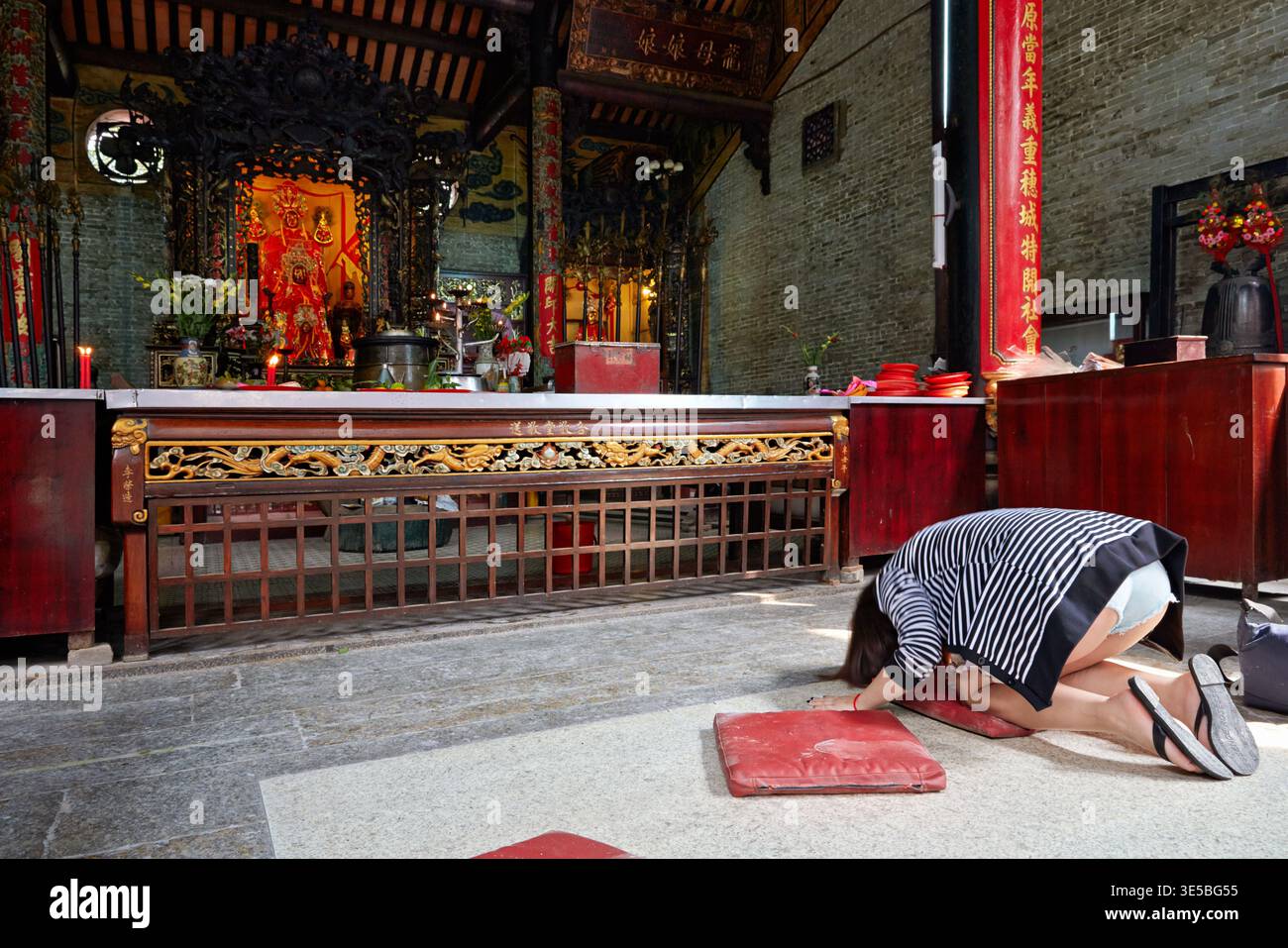 Eine Person kniet im Gebet in einem Tempel in Ho Chi Minh. Der Tempel verfügt über einen Altar mit Opfergaben und Dekorationen. Stockfoto