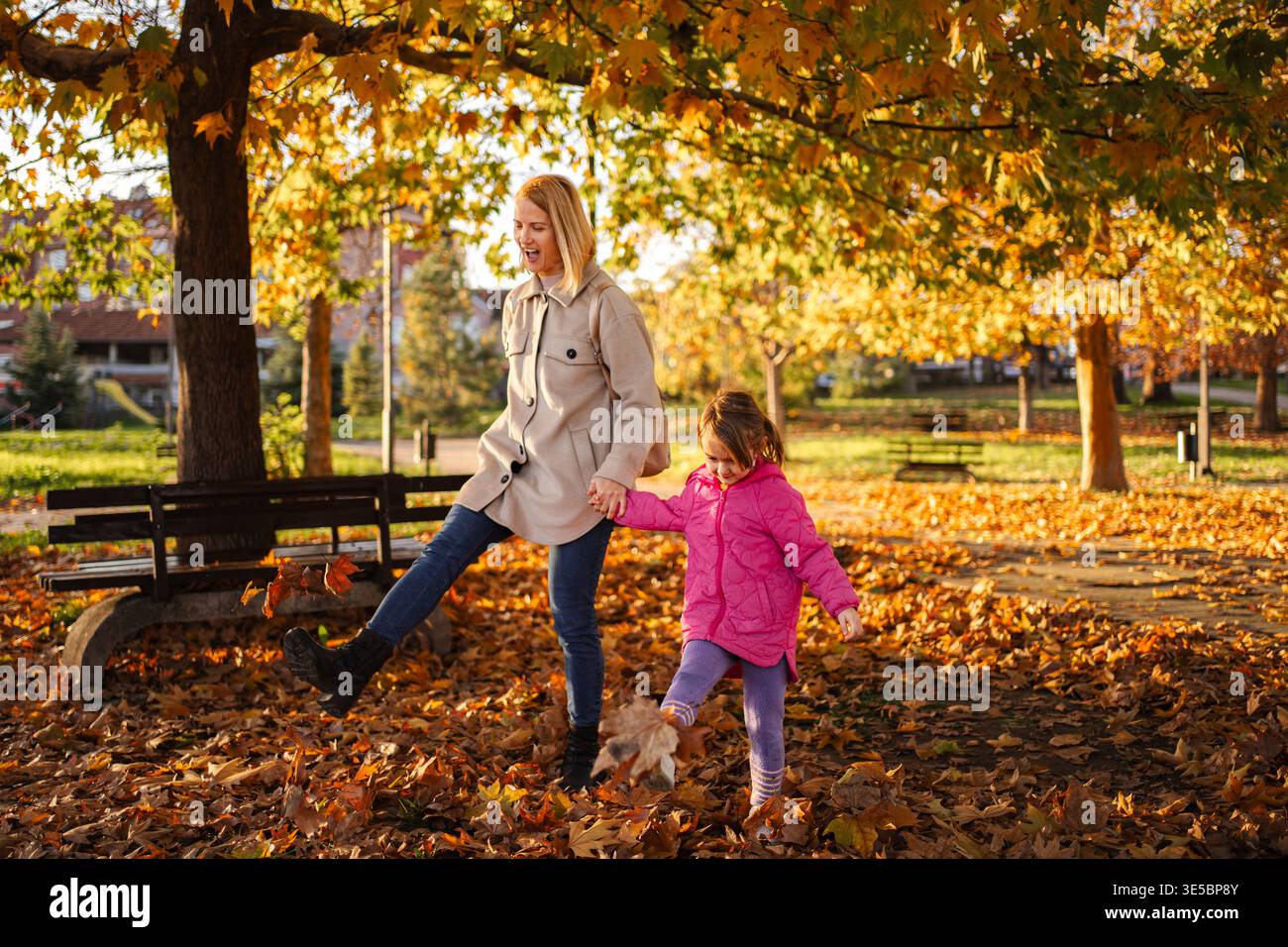Mutter und Tochter spielen draußen und treten Herbstlaub Stockfoto