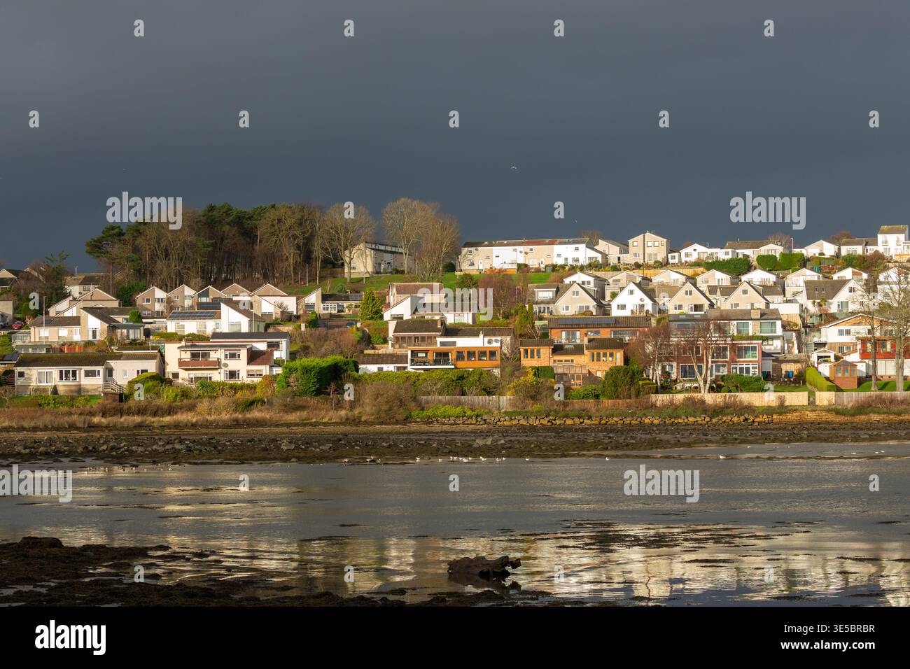 Häuser am Wasser in Dalgety Bay in der Sonne mit dunklem Himmel dahinter, Fife, Schottland Stockfoto