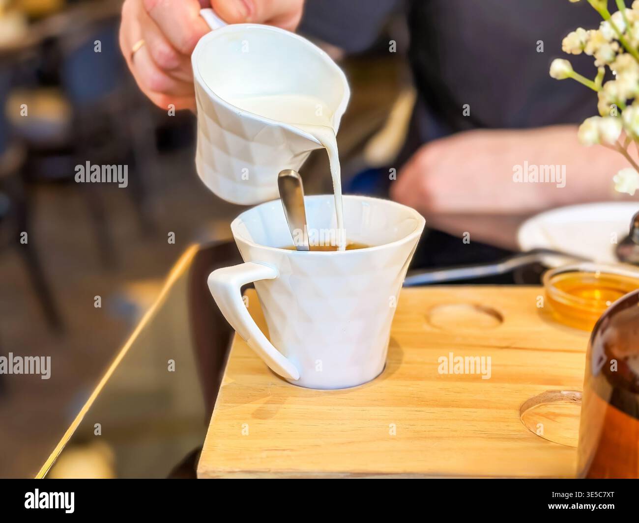 Keramikbecher auf Brunch-Tablett. Elegante Gastfreundschaft mit dampfendem Kaffee und Blumen. Nahaufnahme des Kaffees, der während der Verfeinerung in Tassen gegossen wird Stockfoto