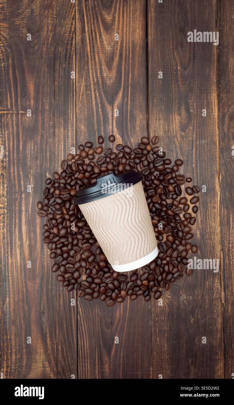 Aromatische geröstete Kaffeebohnen mit nachgebildeter Papiertasse zum Mitnehmen. Dunkler Hintergrund, Draufsicht, Copyspace. Stockfoto