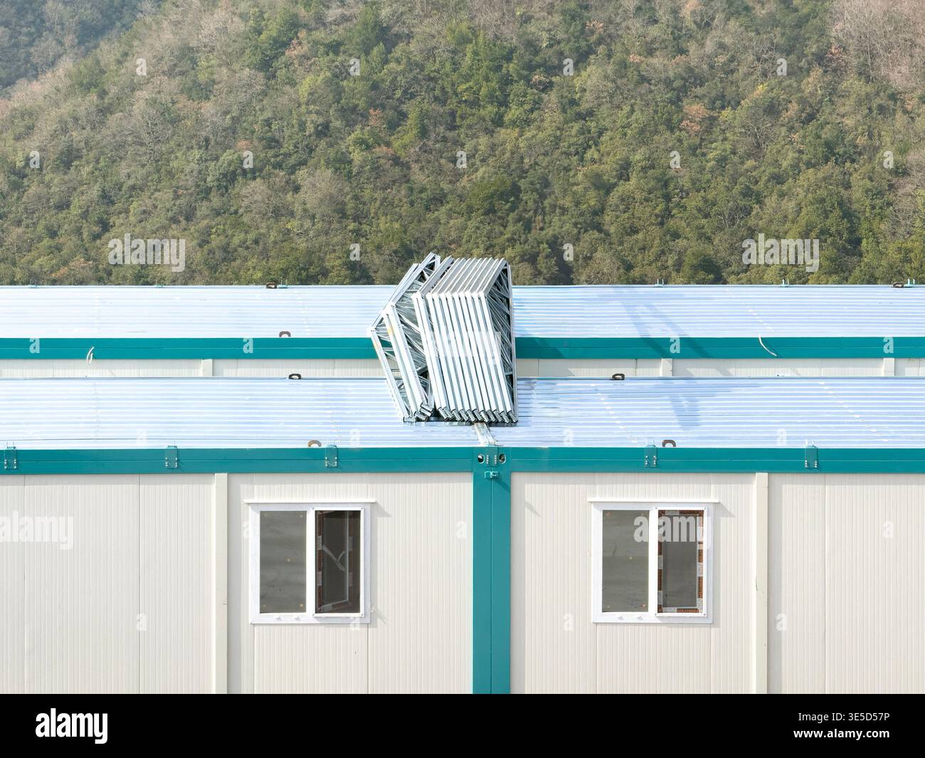 Vorgefertigte Containergebäude mit Metalldächern, vor einer üppigen Bergkulisse, mit effizientem Industriedesign im Einklang mit na Stockfoto