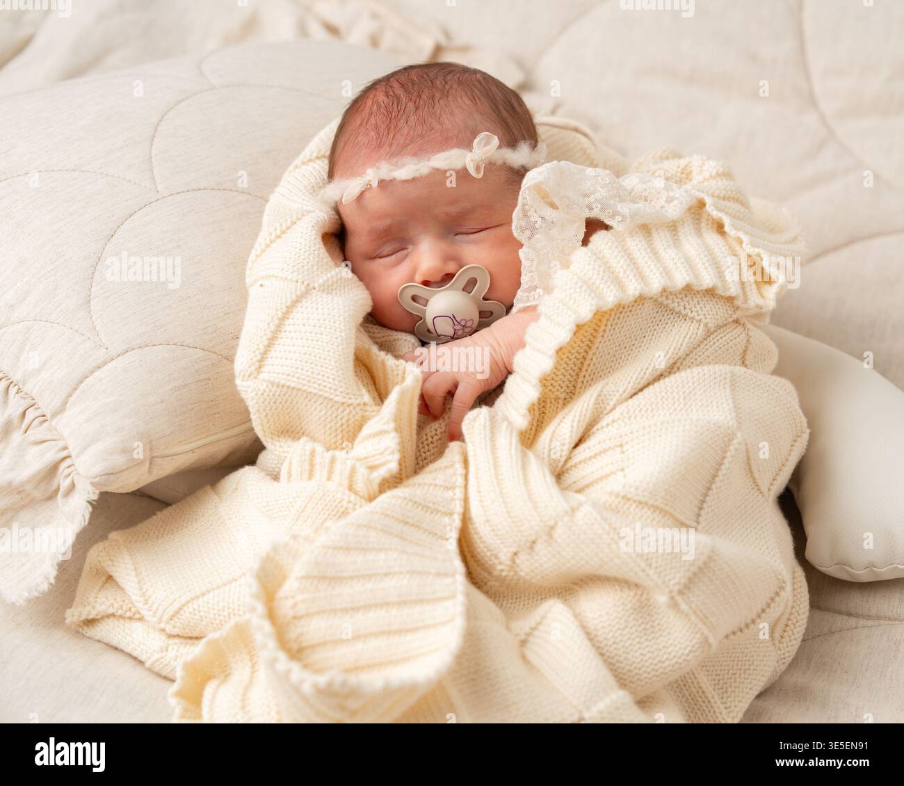 Friedliches Neugeborenes, das in einer kuscheligen Strickdecke schläft. Sanftes natürliches Licht, neutrale Töne und minimalistische Komposition, die Unschuld und Wärme hervorhebt Stockfoto