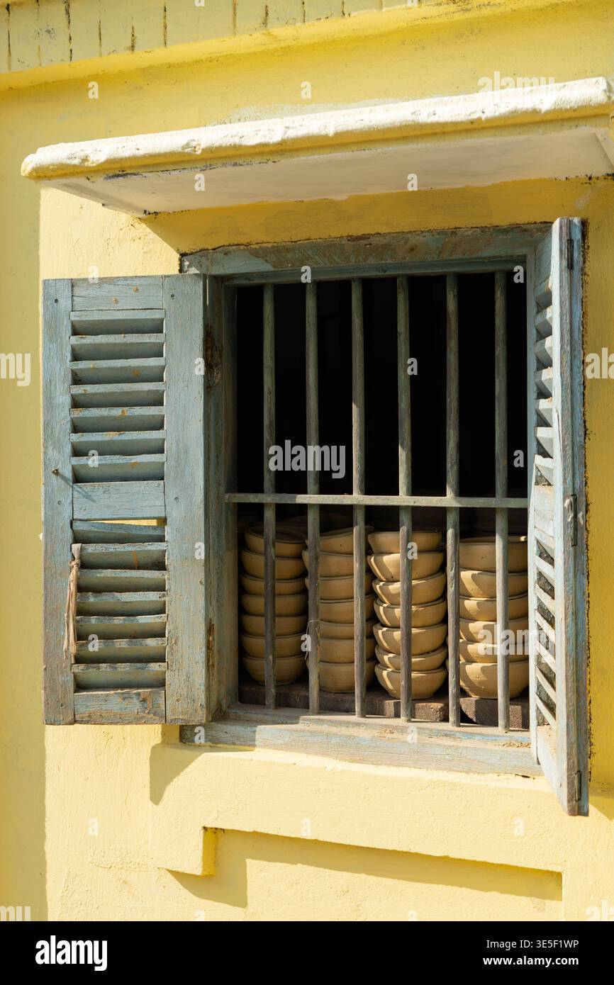 Hoi an, Vietnam - Februar 2026: Töpferschalen hinter Holzfenstern an der Außenfassade des traditionellen Keramikwerkstattgebäudes Stockfoto