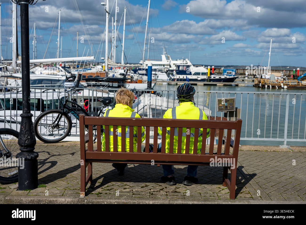 Ein älteres Paar, das gemeinsam auf einer Bank am Yachthafen im Yarmouth Harbour an der Küste der isle of wight, Großbritannien, unterwegs ist Stockfoto