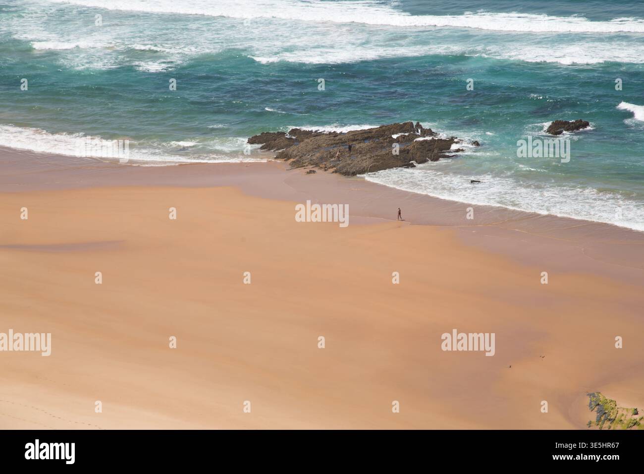Breiter Sandstrand Mit Türkisfarbenen Wellen Und Felsigem Felsvorsprung, Lone Walker On Shore Stockfoto