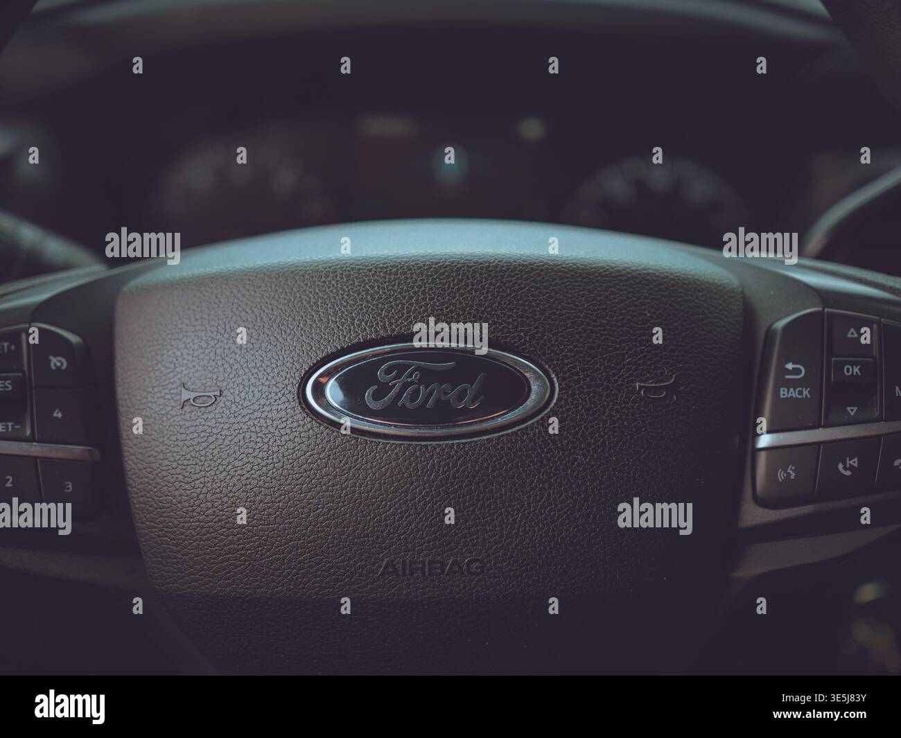 Nahaufnahme einer Ford-Lenkradnabe mit zentralem Logo, Hupensymbolen, Airbag-Markierung und Multifunktionstasten im Fahrzeuginnenraum Stockfoto