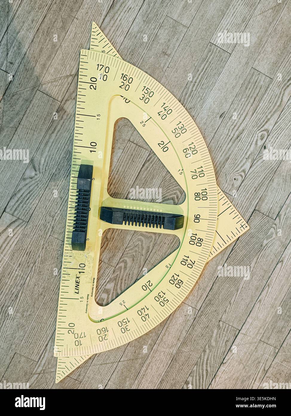 Riga, Lettland - 31. März 2026: Draufsicht auf einen großen transparenten Winkelmesser mit Dreiecklinalen auf Holzboden. Ideal für Ausbildung, Geometrie und Motor Stockfoto