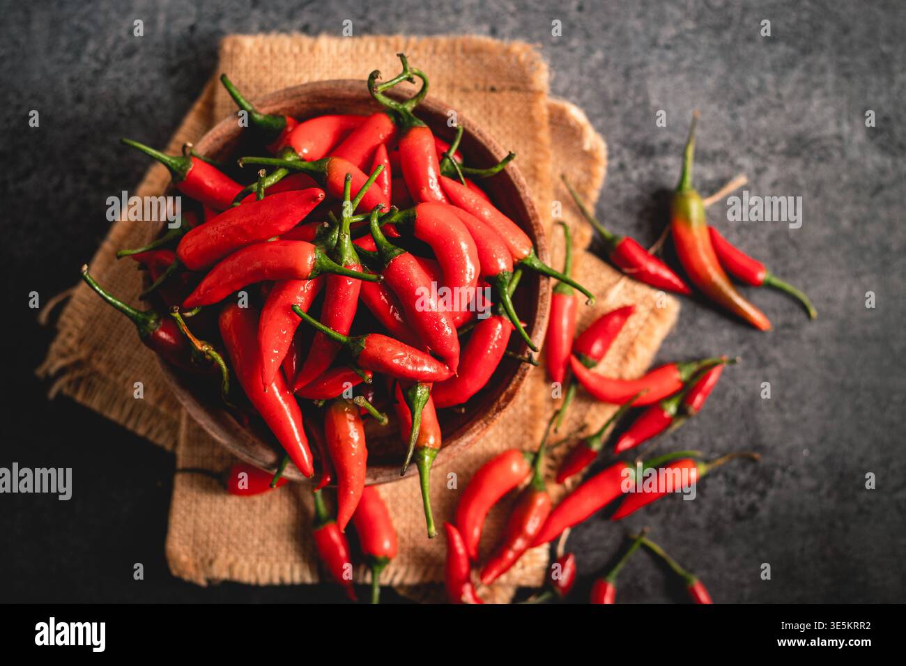 Frische rote Chili-Paprika in rustikaler Holzschale und auf Sackleinen verteilt, lebendige, scharfe Bio-Produkte, Nahaufnahmen von Lebensmitteln mit natürlichem Licht Stockfoto