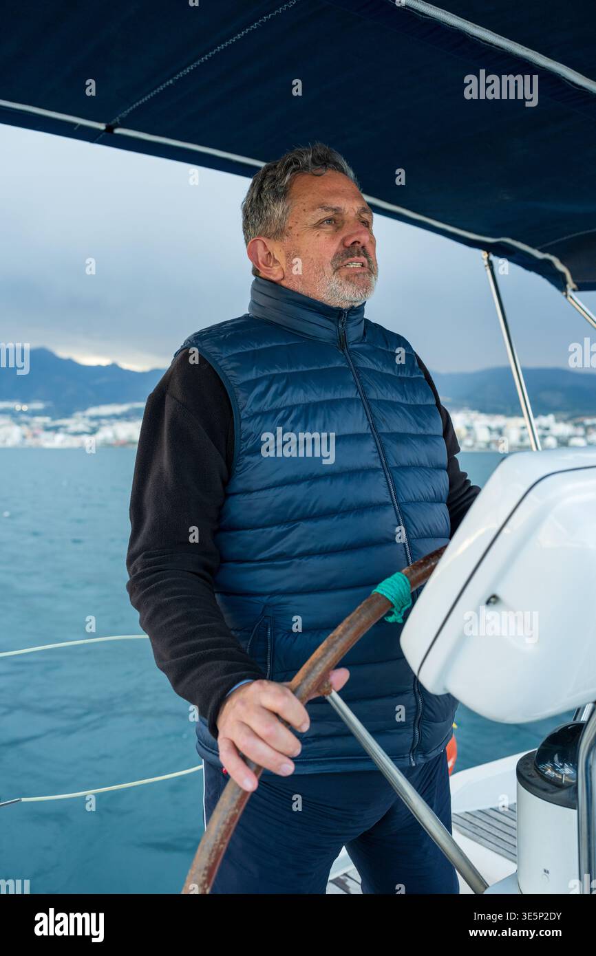 Reifer Mann, der das Segelboot auf der Ozeanreise steuert Stockfoto