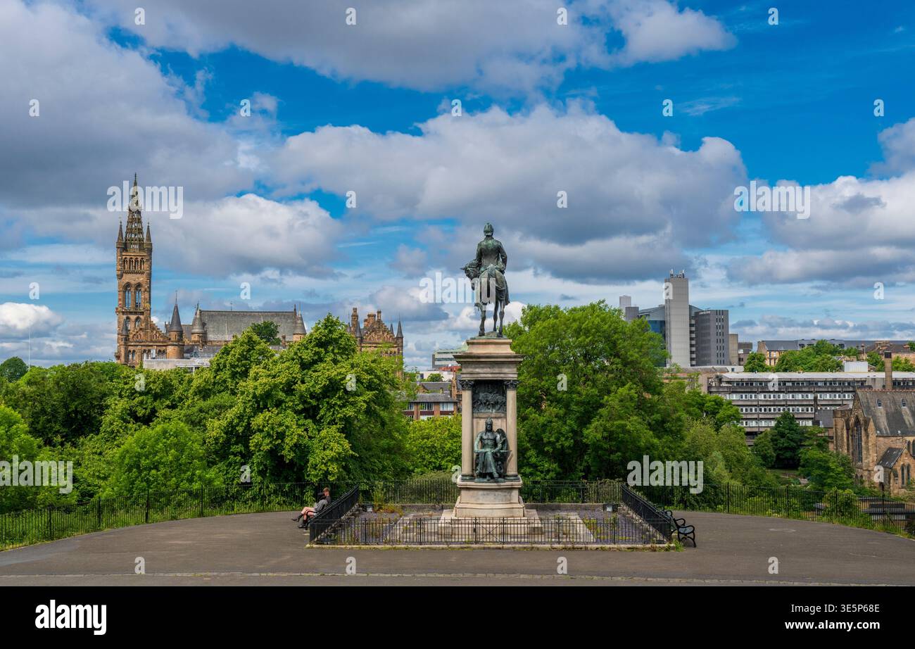 Blick vom Eingang zum Kelvingrove Park mit einer Reiterstatue auf einem Sockel, üppigen Bäumen, historischen Türmbauten und moderner Skyline unter Stockfoto