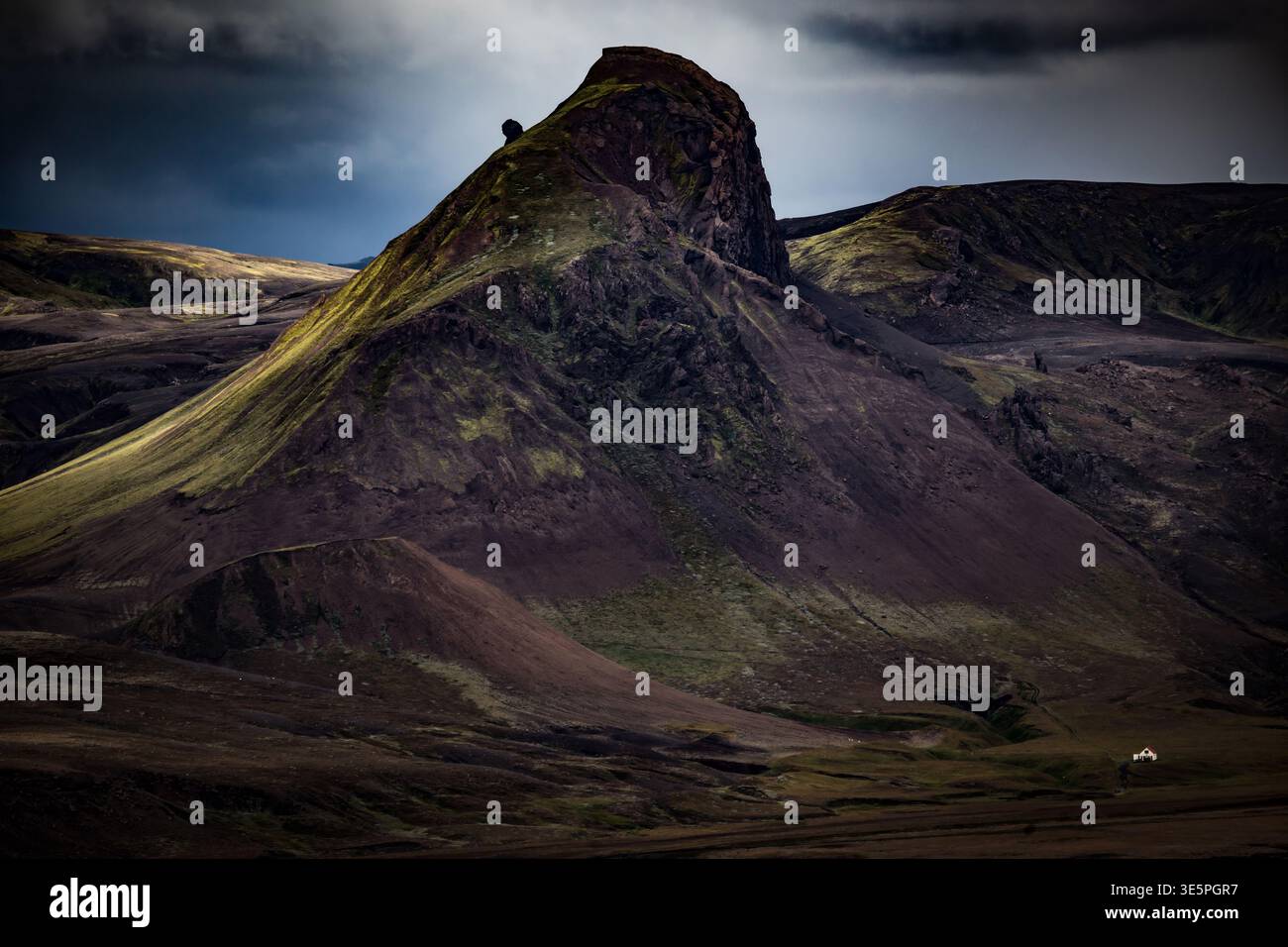 Ein riesiger vulkanischer Berg erhebt sich über einem kleinen Haus in Island Stockfoto