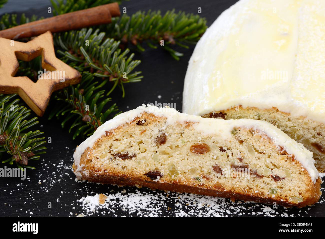 weihnachtsstollen mit Tannenzweig, Sternen und Zimtstäbchen liegen zur weihnachtszeit auf schwarzem Schiefer Stockfoto