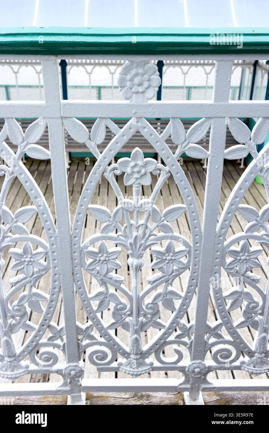 Aus nächster Nähe sehen Sie die kunstvoll verzierte weiße schmiedeeiserne Blumenbalustrade auf einer Seebügellandschaft mit Holzdielen Stockfoto