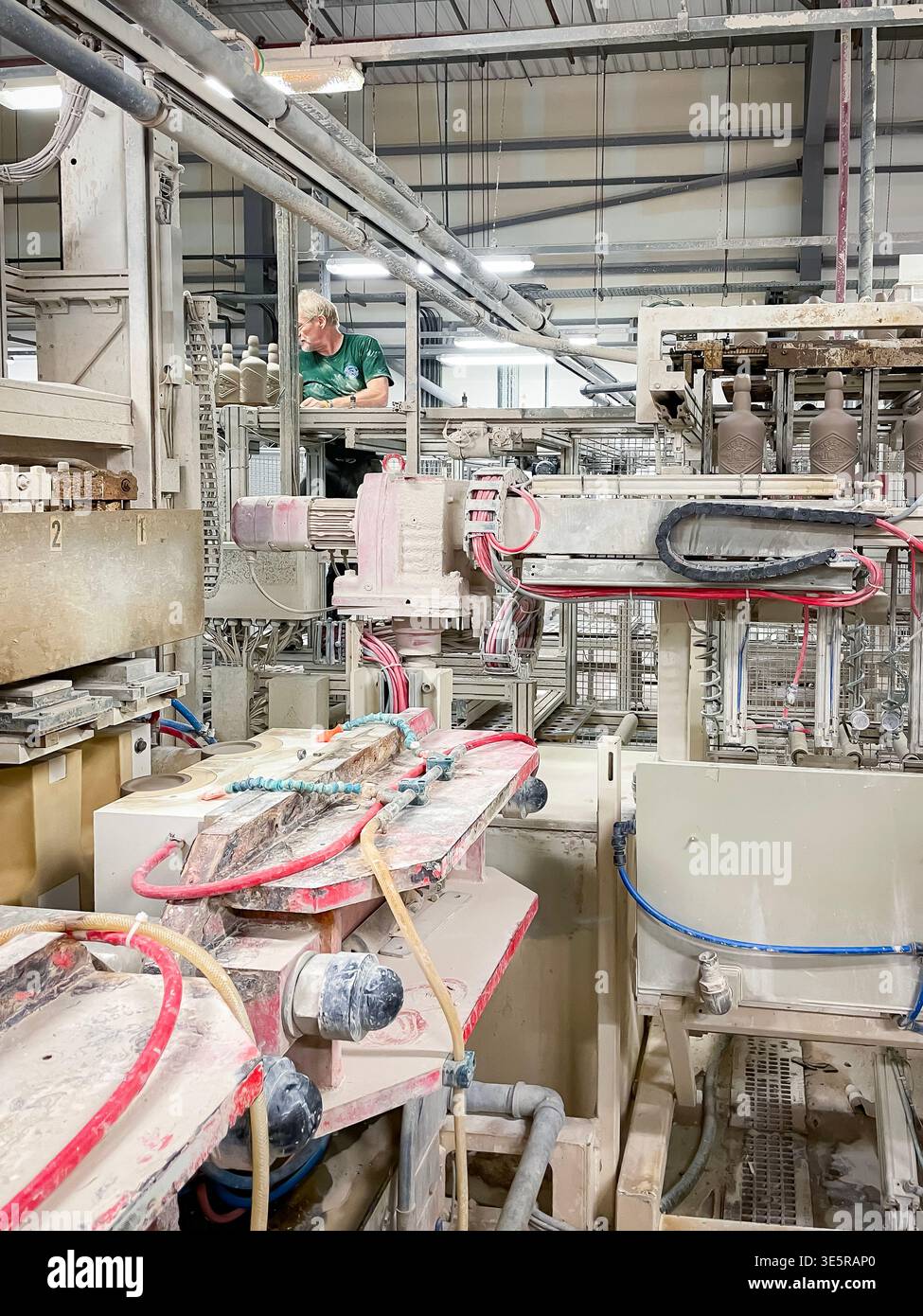 Industrielle Produktionsanlage mit automatisierten Maschinen und einem Mitarbeiter, der den Produktionsprozess in einer Fabrikhalle überwacht Stockfoto