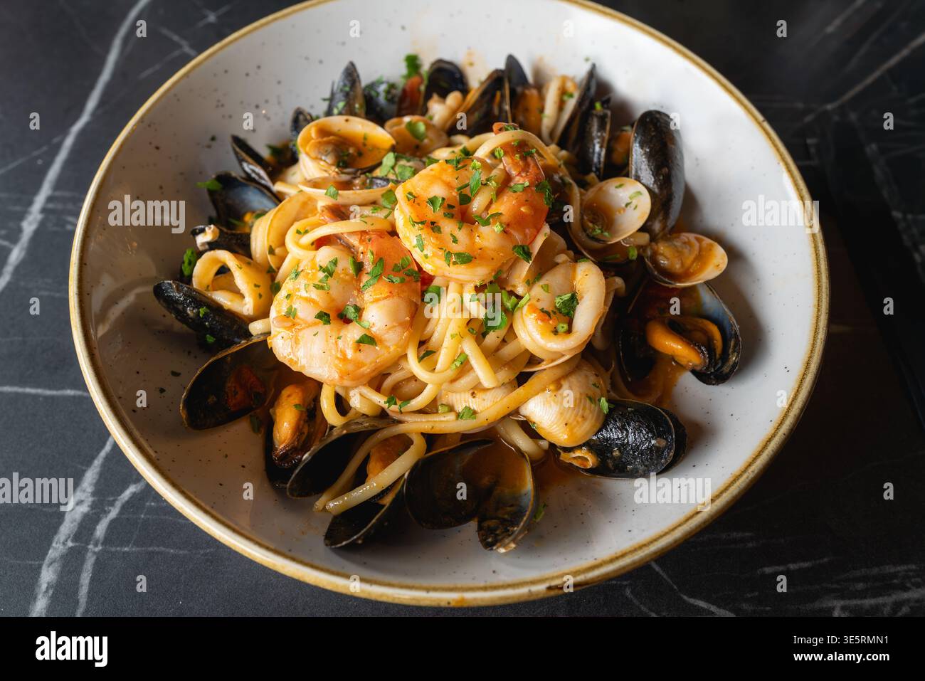 Linguine mit Meeresfrüchten, frischen Calamari, Garnelen, Muscheln und Venusmuscheln, in Weißwein mit Kirschtomaten, garniert mit Petersilie, in einem Gericht mit Stockfoto