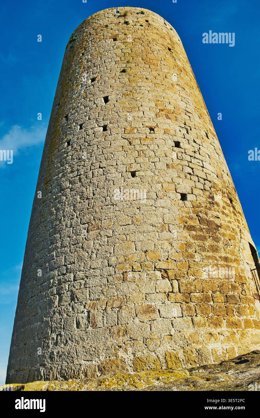Runder mittelalterlicher Turm aus rauem Stein unter einem klaren blauen Himmel in der Stadt Pals, Katalonien, Spanien. Ein alter Steinturm vor einem leuchtend blauen Himmel Stockfoto
