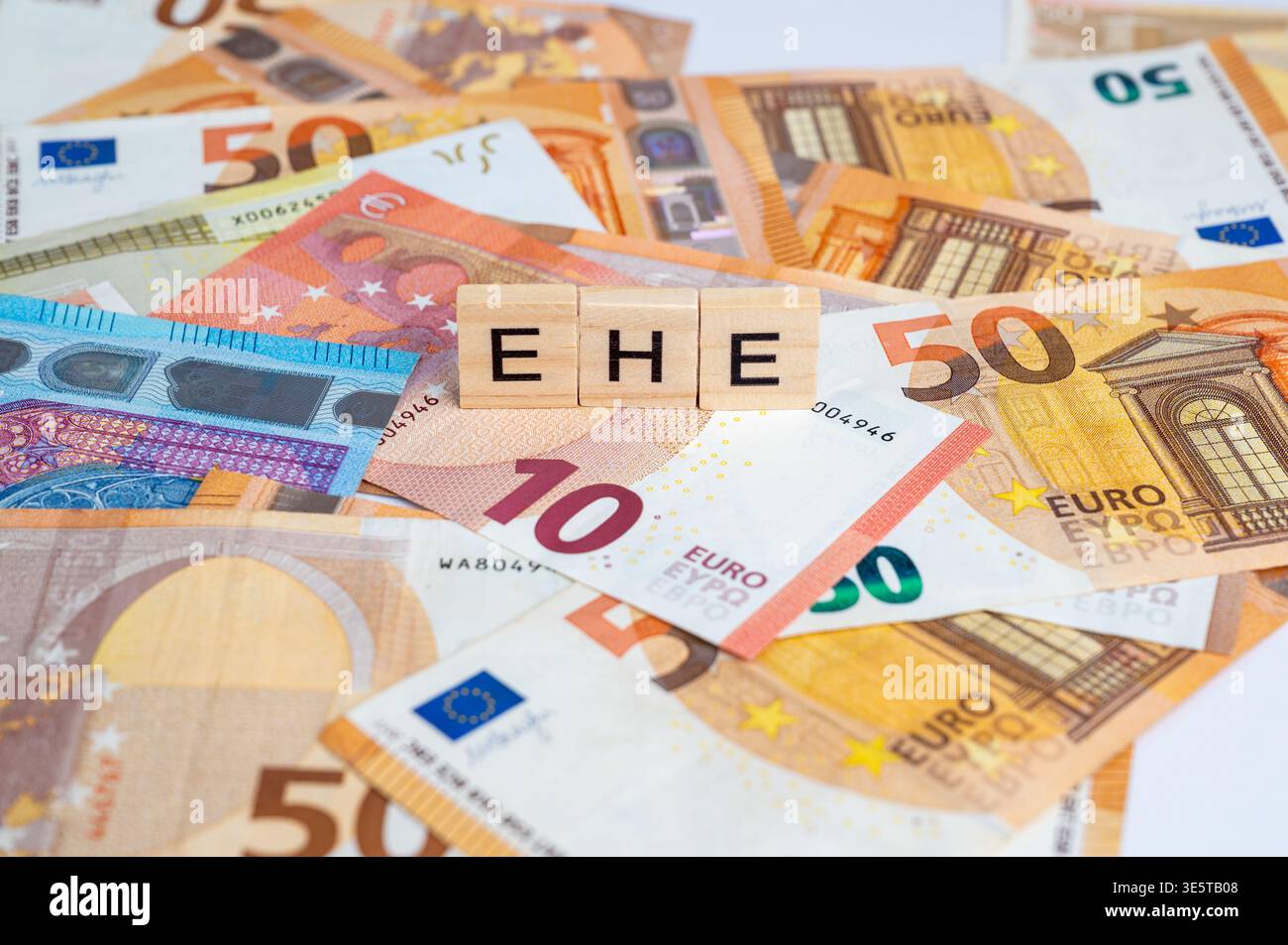 Euro-Banknoten mit drei Holzbuchstaben, die EHE schreiben: Kürzungen bei Heiratsleistungen und Steueraufteilung Stockfoto