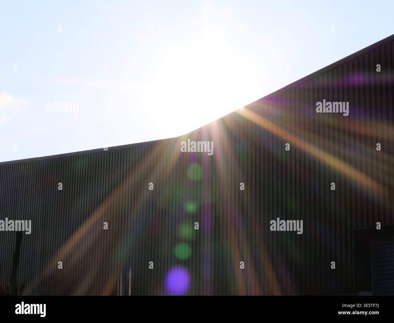 Sonnenlicht über Industriegebäude. Wellblechfassade dunkelgrau. Lichtreflexeffekt bei hellem Sonnenlicht. Moderne Lagerhausarchitektur. Stockfoto