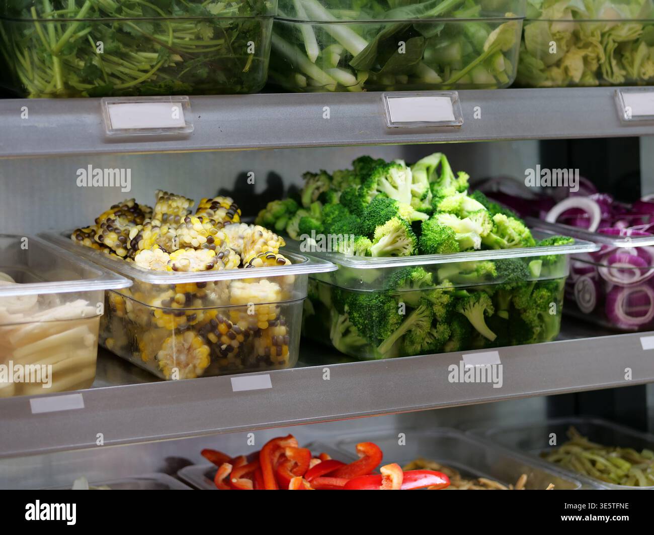 Bei der mittleren Nahaufnahme aus einem hohen Winkel wird ein gekühltes Salatbuffet oder ein Buffet mit frischem, gehacktem Gemüse serviert. Transparente Kunststoffbehälter sind Stockfoto