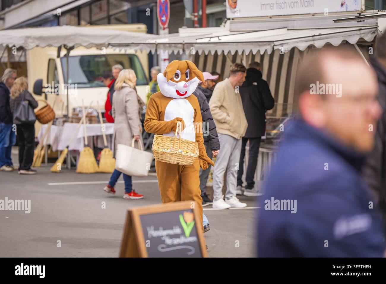 Person, die Osterhasenkostüm auf einem geschäftigen Markt trägt, einen Korb trägt und an Verkaufsständen vorbeiläuft, Osterkampagne, Sindelfingen, Stadtteil Böblingen, G Stockfoto