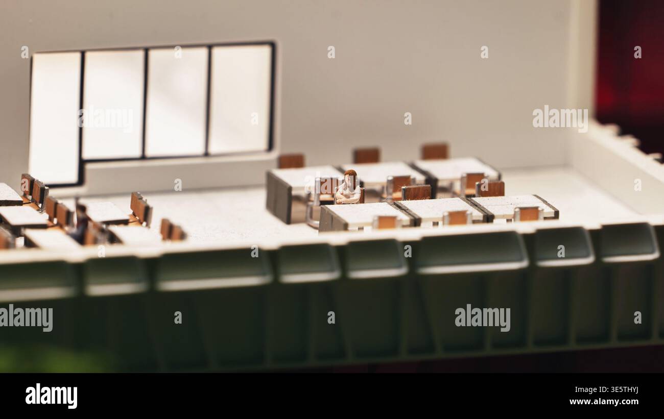 Miniatur-Büro-Diorama mit einer einsamen Frauenfigur, die Einsamkeit am Arbeitsplatz repräsentiert Stockfoto