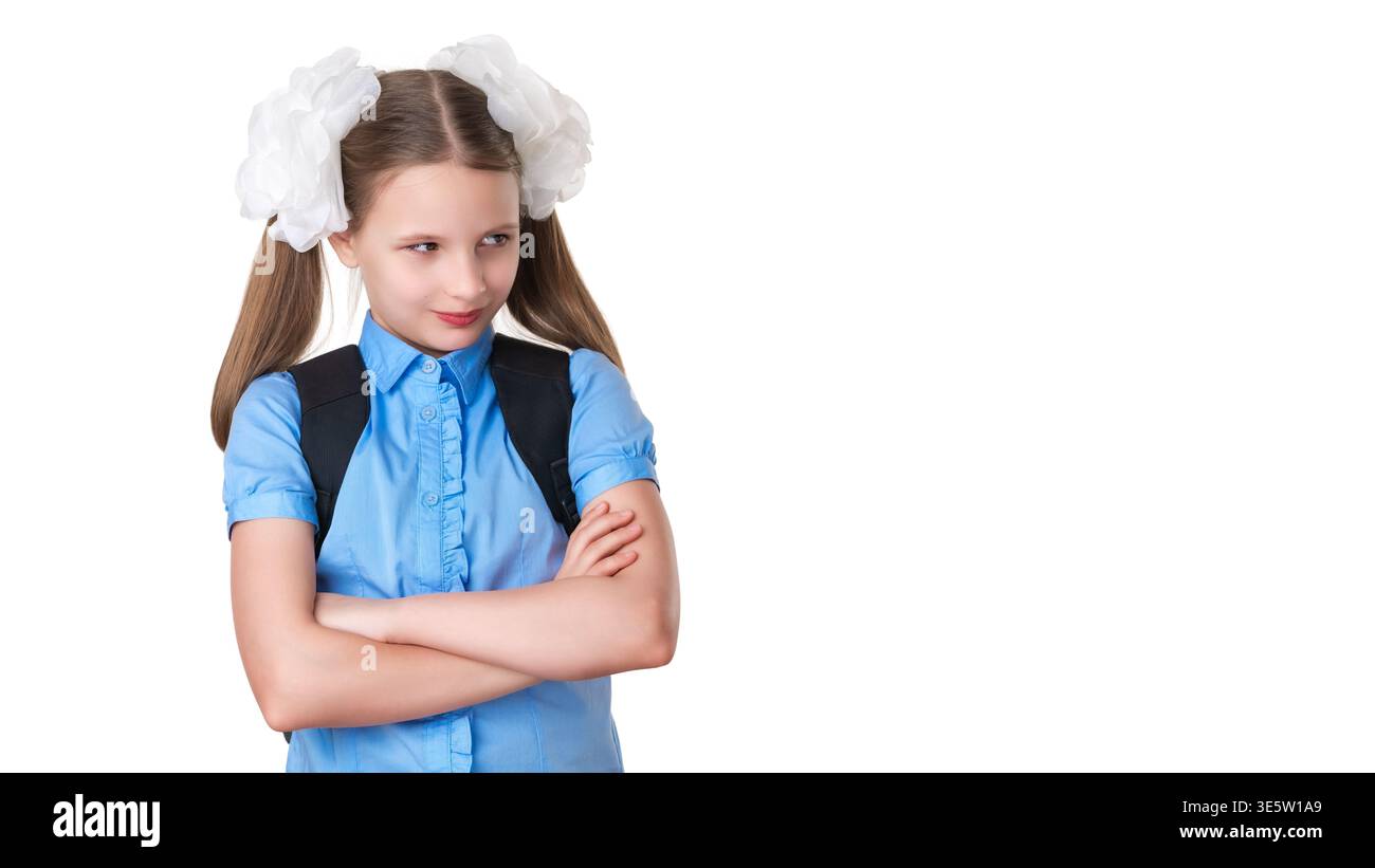 Gerissenes Schulmädchen in blauer Uniform mit Zöpfen und Bögen, Arme überkreuzt. Das Mädchen hat einen Rucksack und sieht seitwärts mit einem schlauen, schelmischen Ausdruck aus. Isol Stockfoto