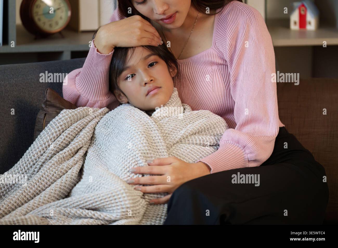 Mutter tröstet ihr krankes Kind auf einer Couch Stockfoto
