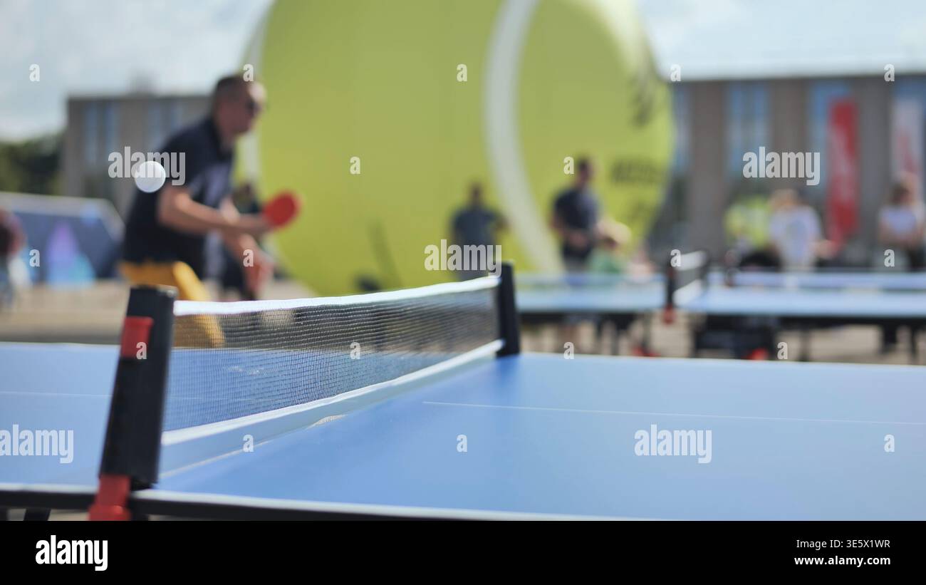 Tischtennisspiel im öffentlichen Raum mit unscharfen Spielern und Riesentennisball Stockfoto