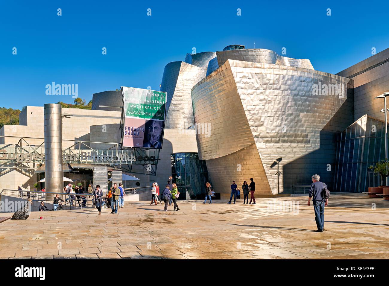 Besucher erkunden das Guggenheim Museum in Bilbao, Spanien, an einem klaren, sonnigen Tag. Das Gebäude zieht viele Touristen an. Stockfoto