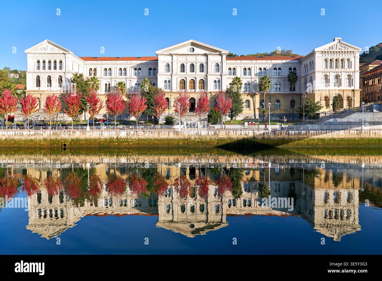 Das Universitätsgebäude befindet sich am Fluss in Bilbao, Spanien. Die Bäume mit roten Blättern stehen vor der Struktur. Stockfoto